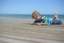 Boy Laying Down On A Wooden Walkway On The Beach