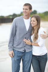 Wall Mural - A beautiful happy young caucasian couple smiling and walking barefoot on the beach.