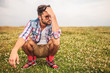 crouched casual man in a grass field thinking
