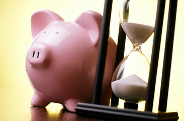 Wall Mural - Pink piggy bank with a vintage hourglass behind