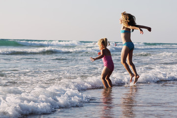 two happy kids playing on the beach at sunset