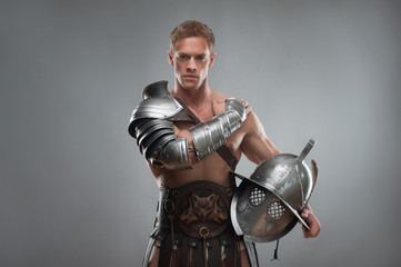 Gladiator in armour posing with helmet over grey background