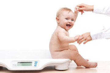 baby sitting on scales and holding hands.