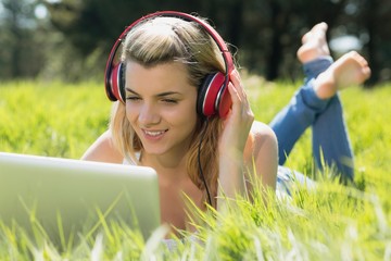 Poster - Pretty blonde lying on grass using laptop listening to music