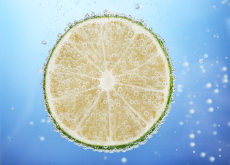 Wall Mural - Fresh lime in water with bubbles on blue background