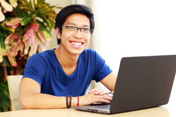 Cheerful asian man sitting at the table with laptop