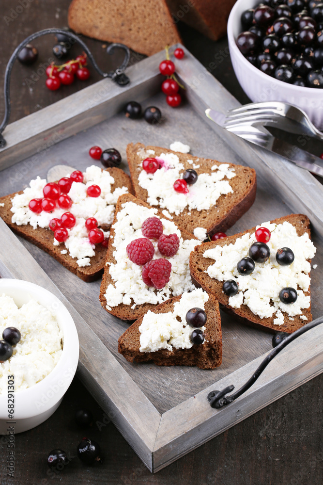 Bread with cottage cheese and berries on wooden tray close-up