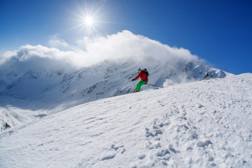 Skier skiing downhill in high mountains against sunset