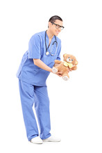 Full Length Portrait Of A Young Male Doctor Giving A Teddy Bear