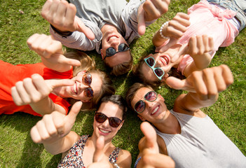 Wall Mural - smiling friends showing thumbs up lying on grass