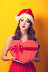 Beautiful brunette girl in christmas hat with gift on yellow bac