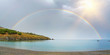 Panorama of a rainbow half over sea and land