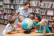 © WavebreakmediaMicro - Cute pupils and teacher looking at globe in library
