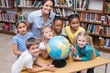 © WavebreakmediaMicro - Cute pupils and teacher looking at globe in library