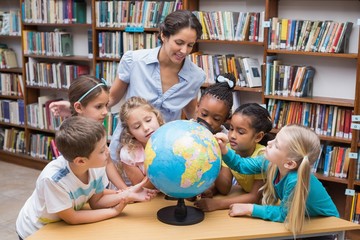 Wall Mural - Cute pupils and teacher looking at globe in library