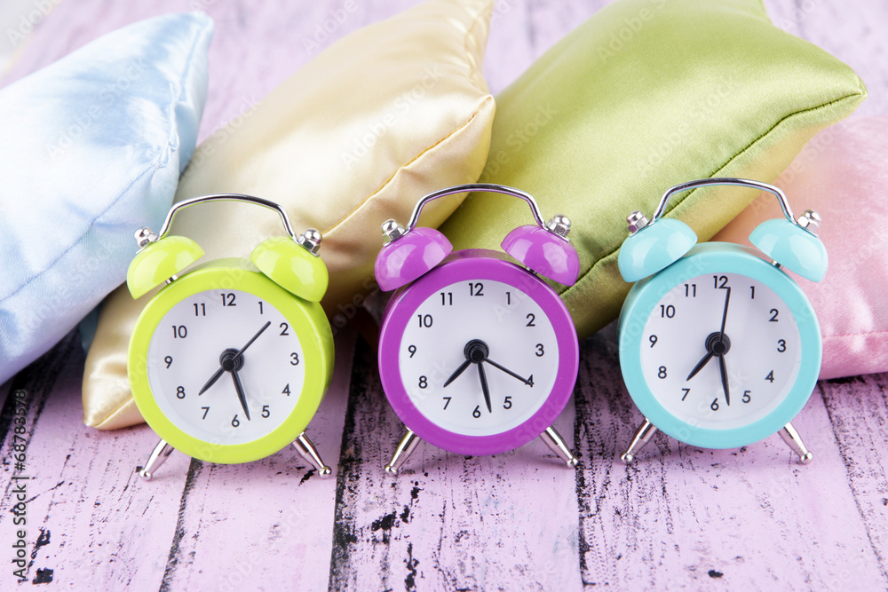 Plastic clocks on a silk pillows on wooden background