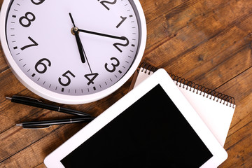 Tablet, cup of coffee, notebook and clock on wooden background