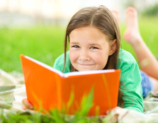 Wall Mural - Little girl is reading a book outdoors