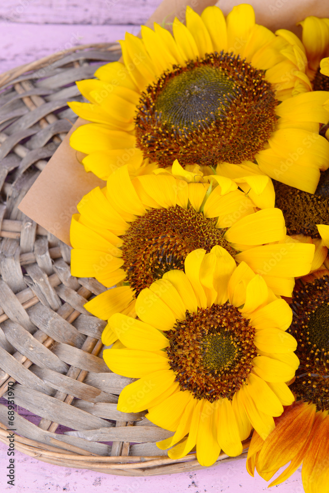 Beautiful sunflowers on wicker stand on table close up