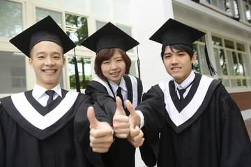 Three graduates are sitting on the grass and thumbs up on campus