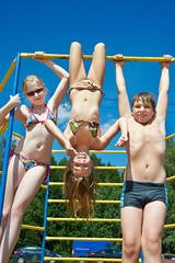 three cheerful children on bar at the playground
