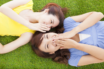 two asian sisters whispering gossip on the grass