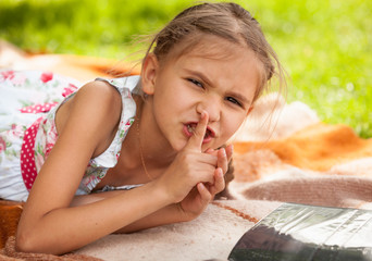 little girl lying at park and holding finger at lips
