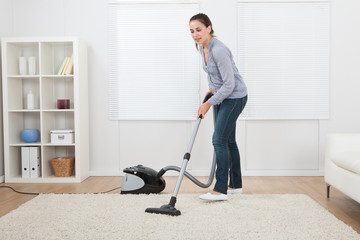 Woman Vacuuming Rug At Home