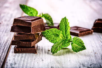 A few cubes of black chocolate with mint leaves on wooden table