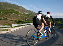 Cyclists On A Tandem Bicycle Riding Uphill On A Mountain Roadway