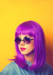 Beautiful girl with violet hair in sunglasses on yellow backgrou