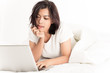 © Nonwarit - Smiling woman using a laptop while lying on her bed