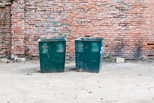Two Green Dustbins Outside Against Red Brick Wall