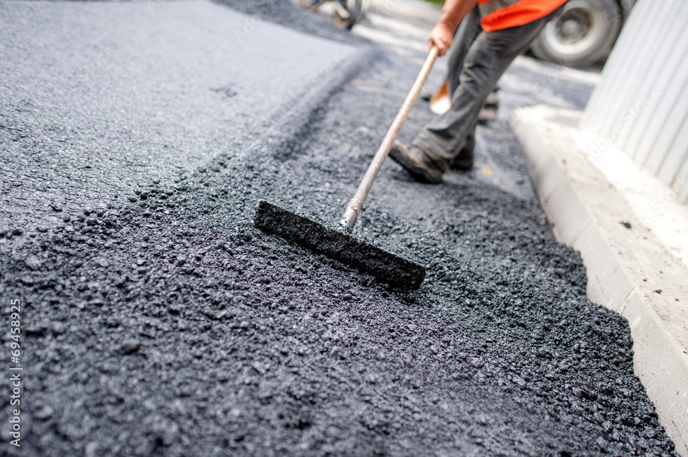 Worker leveling fresh asphalt on a road building - obrazy, fototapety, plakaty 