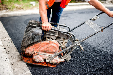 asphalt worker at road construction site with compactor plate