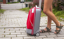 Travel Concept, The Girl's Legs And Red Suitcase Outdoors.