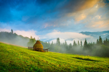 Wall Mural - amazing mountain landscape with fog and a haystack