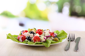 Greek salad in plate on wooden table on natural background