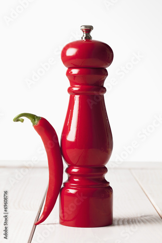 Fotografía Rote Peperoni, rote Pfeffermühle auf weissem Holztisch