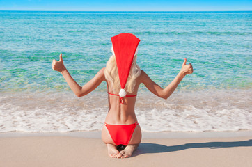 Wall Mural - Beautiful blonde woman in red christmas hat on sea beach.