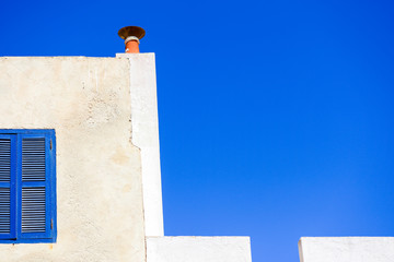 A piece of blue window on a piece of white wall on blue sky