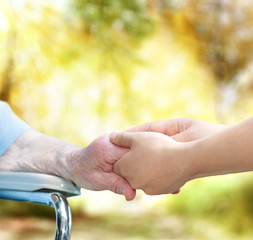 Wall Mural - Senior lady in wheel chair holding hands with young caretaker