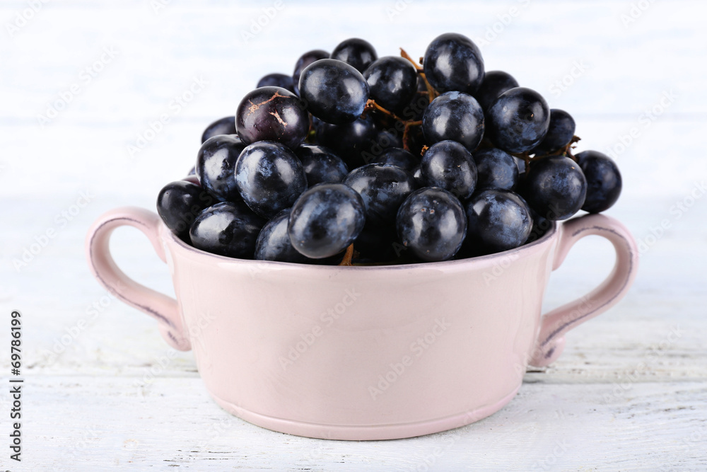Purple grapes in bowl on wooden background