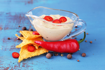 Tasty nachos and bowl with sauce on color wooden background