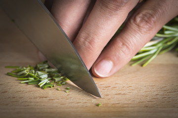 Cocinero picando romero a cuchillo en la mesa de la cocina