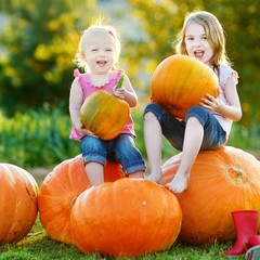 two little sisters sitting on huge pumpkins
