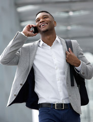 Smiling young man walking and talking on mobile phone