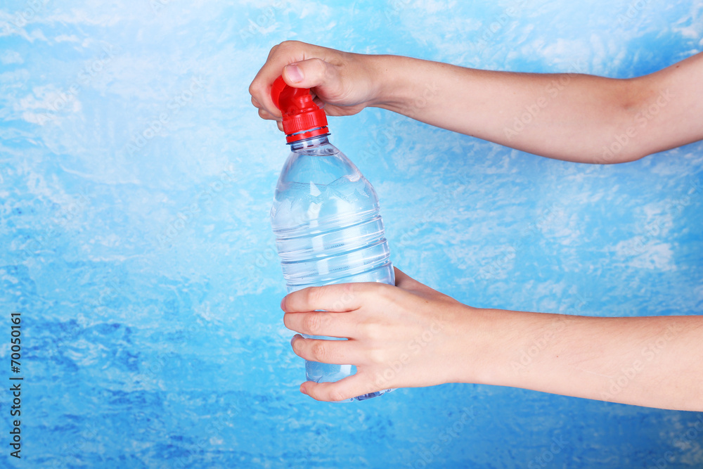 Hand holds bottle with water on blue background