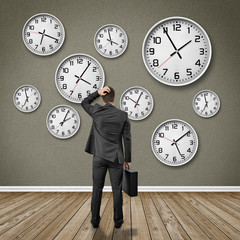 Wall Mural - Man stands in front of a wall with clocks