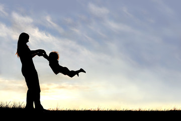 silhouette of mother playing with child outside at sunset